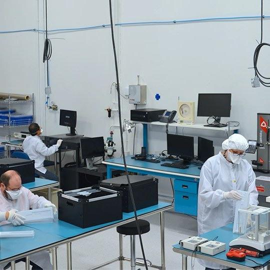 Three employees dressed in white lab unforms working on space technology